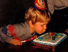 Young Seth Alberty blowing out the birthday candles on his cake wearing a birthday hat