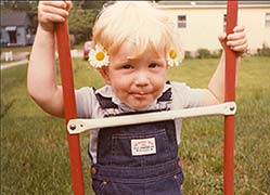 Young Seth Alberty with flowers in his hair wearing overall jeans