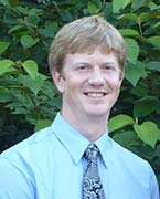 Portrait of Seth Alberty wearing tie and standing in front of green leaves